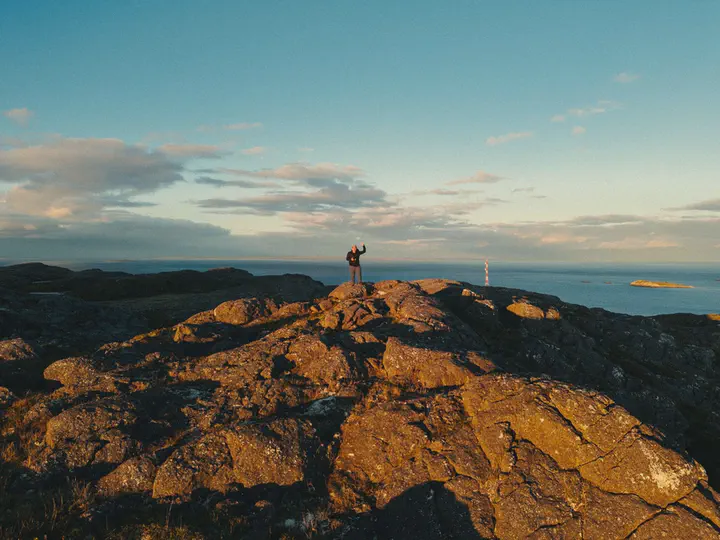 Une silhouette seule debout sur un plateau rocheux au bord de la mer, dans la lumière rasante du soir.