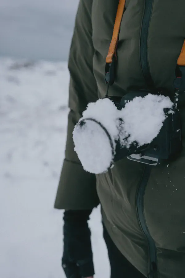 Un appareil photo couvert de neige, suspendu à sa sangle sur une veste kaki.